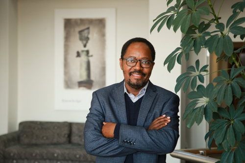 The Dean leans against a column, smiling at the camera