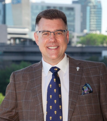 professor with spectacles, wearing a brown jacket and blue/gold tie