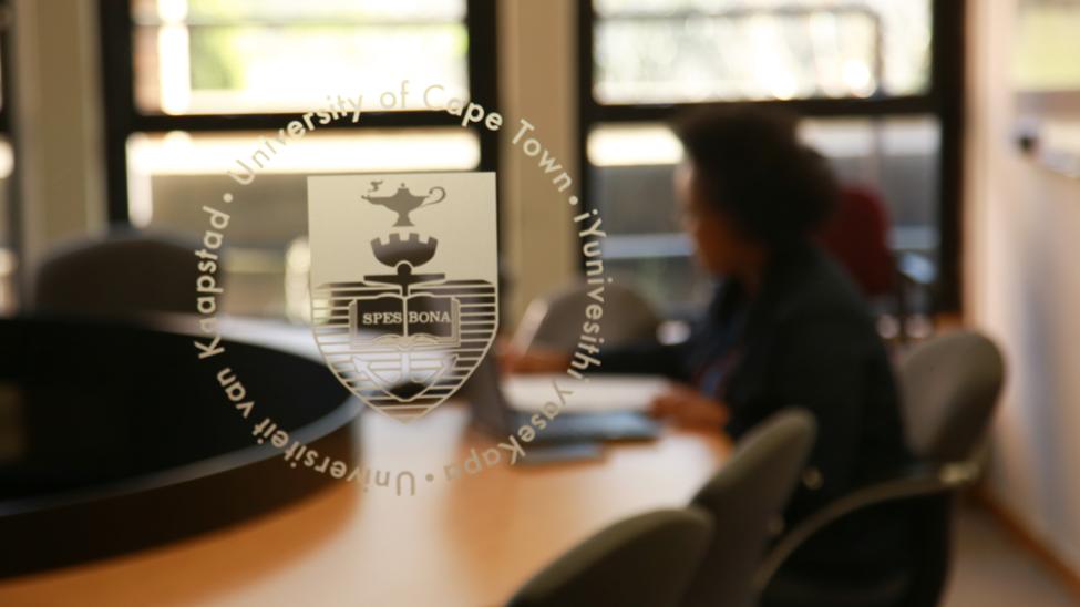 Woman seated at desk seen through window with UCT logo