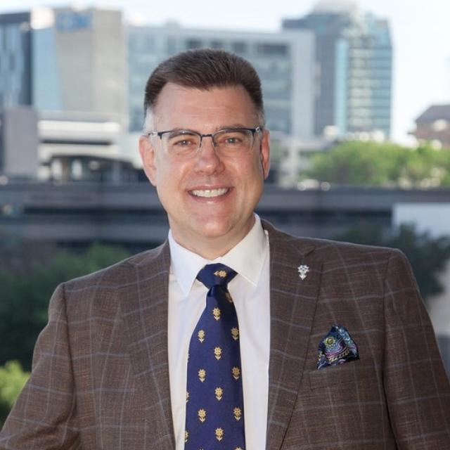 Professor sitting facing camera with brown jacket and blue gold tie