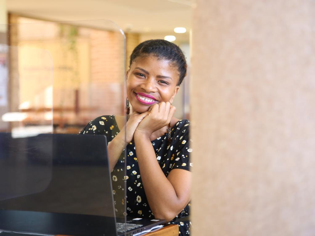 student smiles at camera in front of laptop